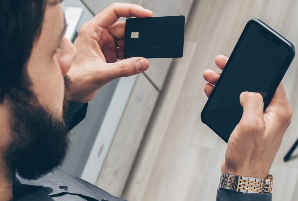 Adult man using a smartphone for online transactions while holding a credit card indoors.